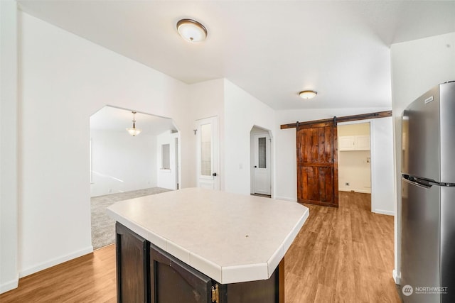 kitchen featuring dark brown cabinetry, stainless steel fridge, a kitchen island, a barn door, and light hardwood / wood-style floors