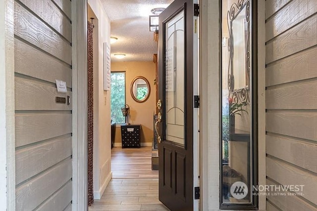 hallway featuring light wood-style flooring, baseboards, and a textured ceiling