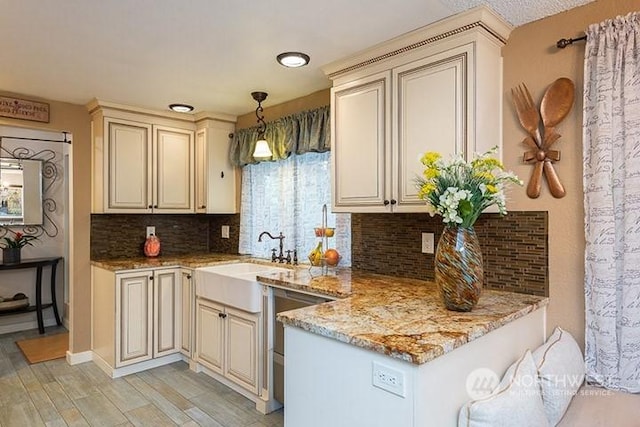 kitchen with a peninsula, light stone countertops, cream cabinets, a sink, and backsplash