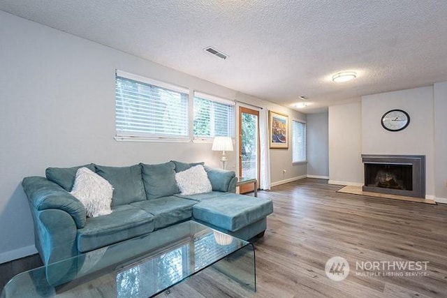 living room featuring baseboards, visible vents, a fireplace with raised hearth, wood finished floors, and a textured ceiling