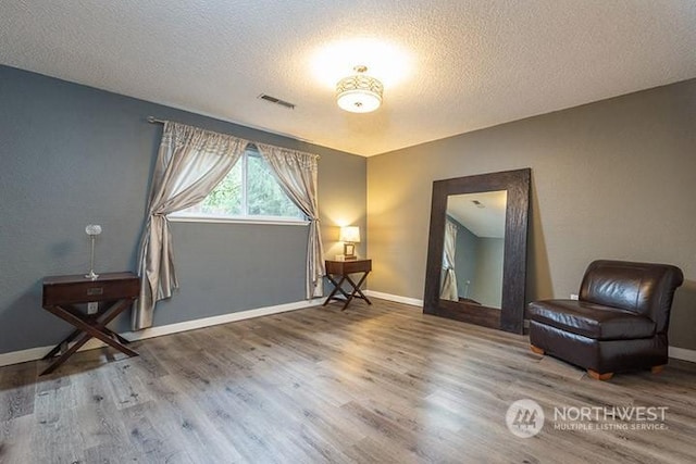 sitting room with visible vents, a textured ceiling, baseboards, and wood finished floors