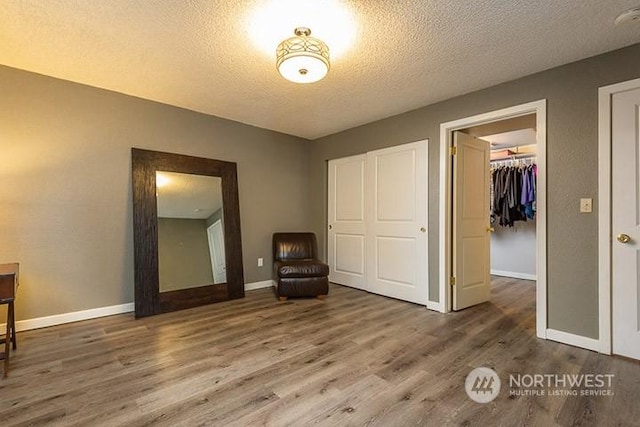 unfurnished bedroom featuring a textured ceiling, a spacious closet, a closet, and wood finished floors