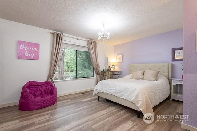 bedroom with a textured ceiling, baseboards, wood finished floors, and an inviting chandelier