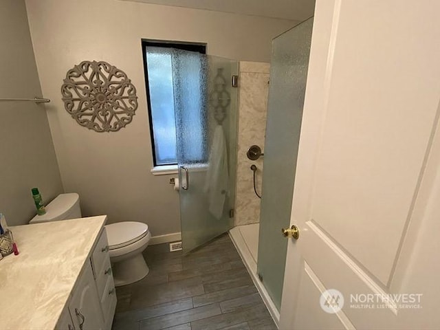 bathroom featuring baseboards, toilet, wood finished floors, vanity, and a shower stall