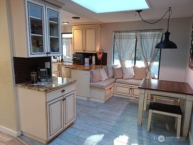 kitchen with light stone countertops, stainless steel dishwasher, decorative backsplash, light wood finished floors, and glass insert cabinets