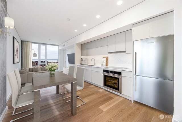 kitchen with tasteful backsplash, sink, white cabinets, light hardwood / wood-style floors, and stainless steel appliances