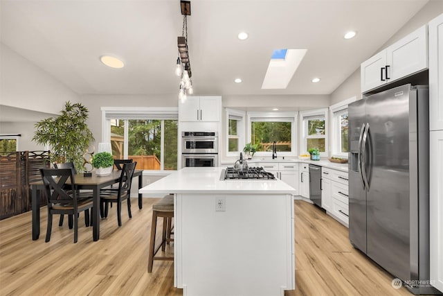 kitchen with white cabinetry, a skylight, a center island, appliances with stainless steel finishes, and a kitchen breakfast bar