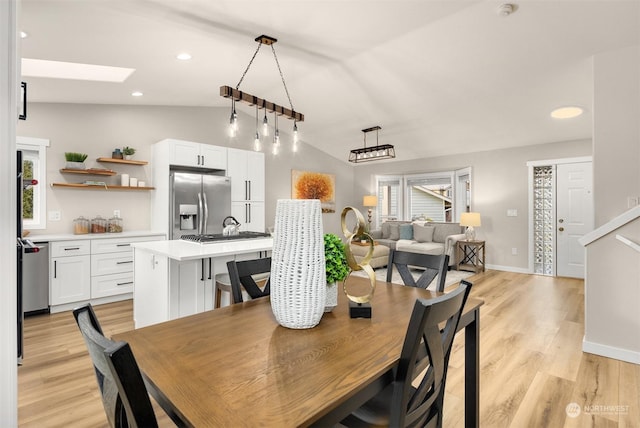 dining area featuring lofted ceiling with skylight and light hardwood / wood-style floors