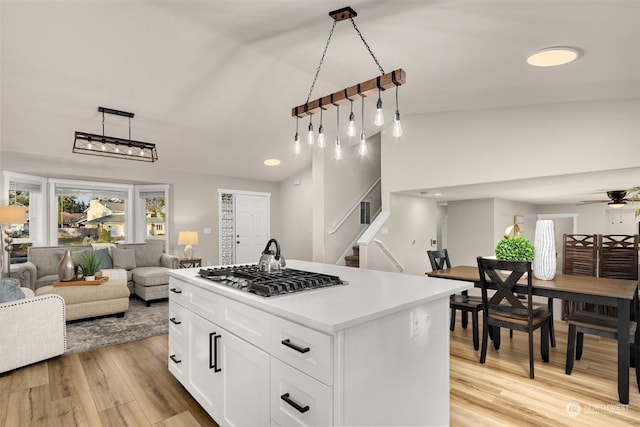 kitchen with a center island, pendant lighting, stainless steel gas stovetop, light hardwood / wood-style floors, and white cabinets