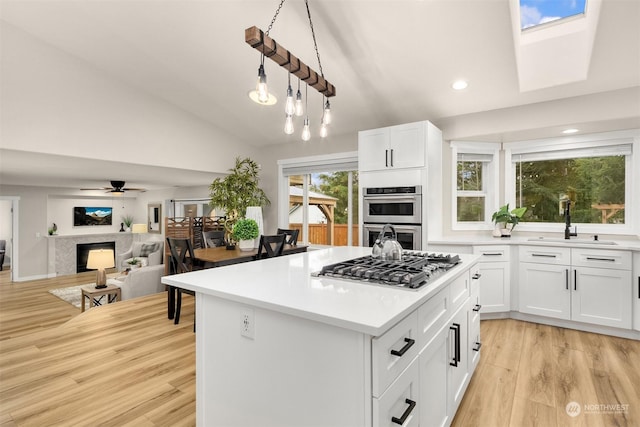 kitchen featuring vaulted ceiling, light hardwood / wood-style flooring, pendant lighting, stainless steel appliances, and white cabinets