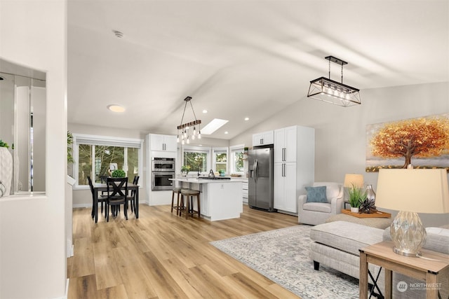 living room with high vaulted ceiling, a skylight, and light hardwood / wood-style floors