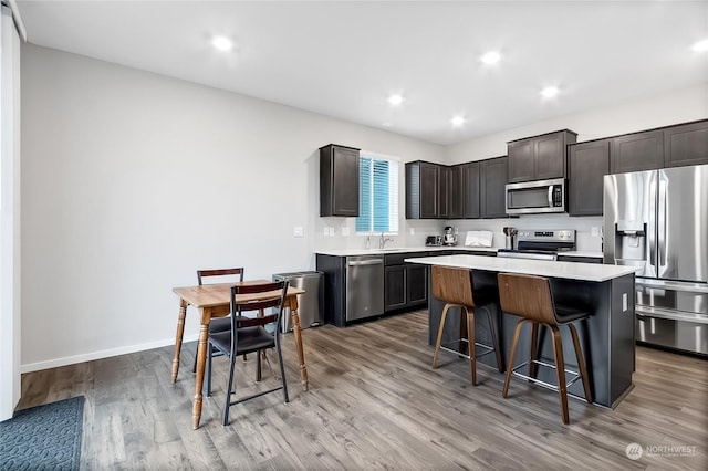 kitchen with dark brown cabinetry, a breakfast bar area, light wood-type flooring, a kitchen island, and stainless steel appliances