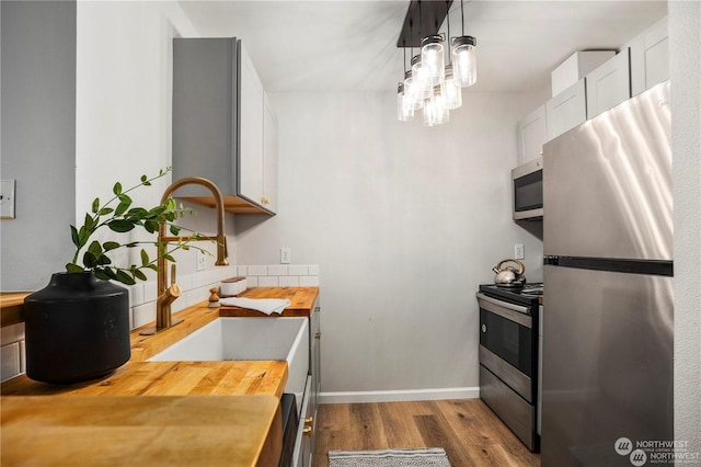 kitchen featuring pendant lighting, white cabinetry, wooden counters, light hardwood / wood-style floors, and stainless steel appliances