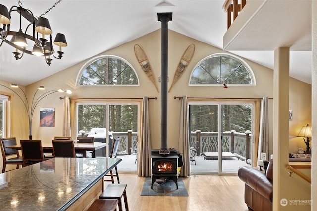 dining area with a notable chandelier, light wood-type flooring, high vaulted ceiling, and a wood stove