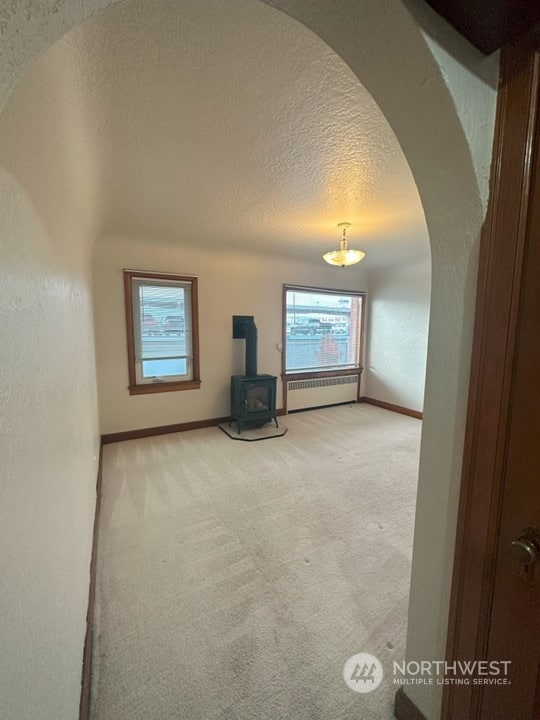 interior space featuring radiator heating unit, a wood stove, light colored carpet, and a textured ceiling