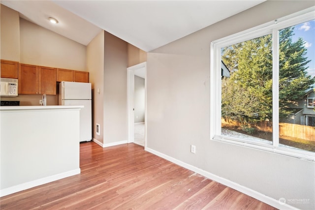 kitchen with white appliances, vaulted ceiling, and light wood-type flooring