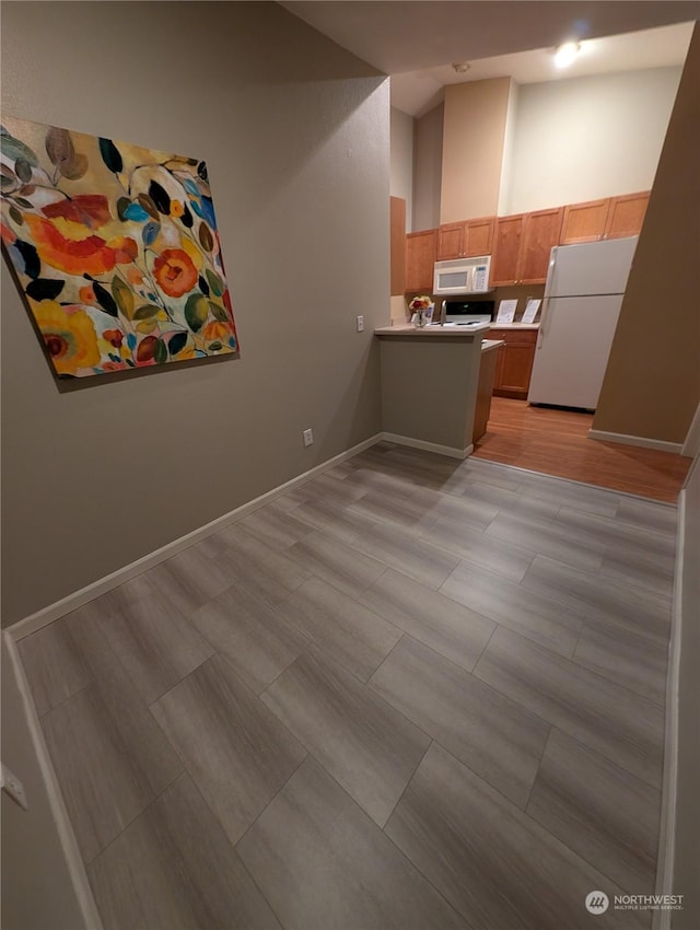 kitchen featuring a towering ceiling, white appliances, and kitchen peninsula