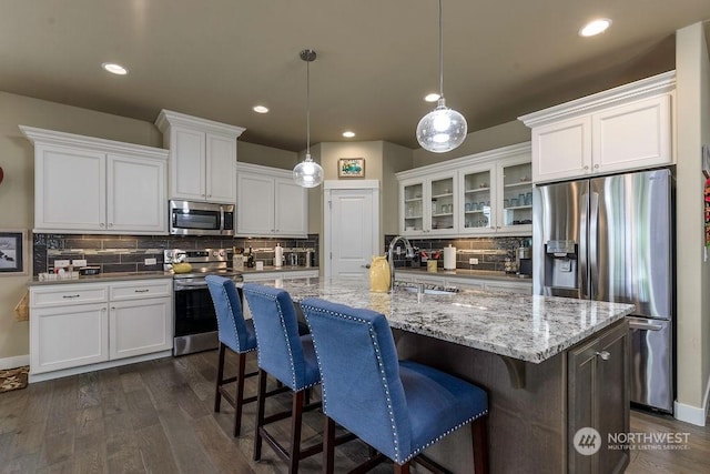 kitchen featuring appliances with stainless steel finishes, white cabinets, hanging light fixtures, a kitchen island with sink, and dark wood-type flooring