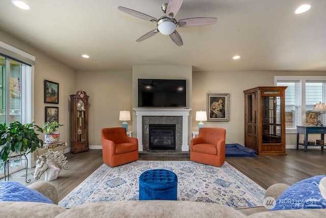 living room with a tiled fireplace, dark wood-type flooring, and ceiling fan