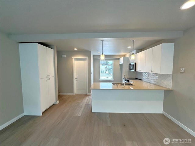 kitchen featuring a peninsula, white cabinetry, hanging light fixtures, light countertops, and stainless steel microwave