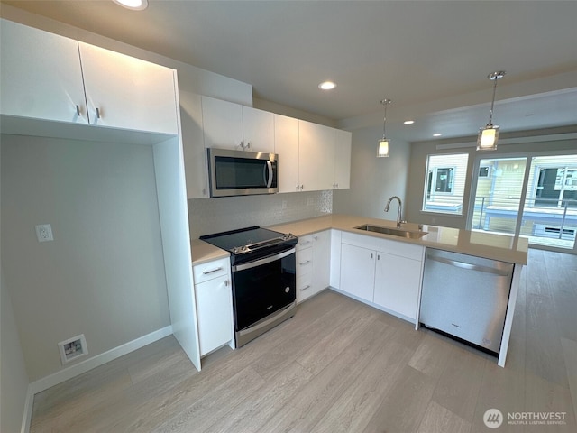 kitchen featuring white cabinets, hanging light fixtures, stainless steel appliances, light countertops, and a sink