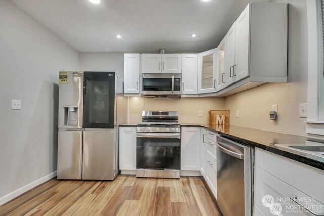 kitchen with dark stone countertops, stainless steel appliances, light hardwood / wood-style floors, and white cabinets