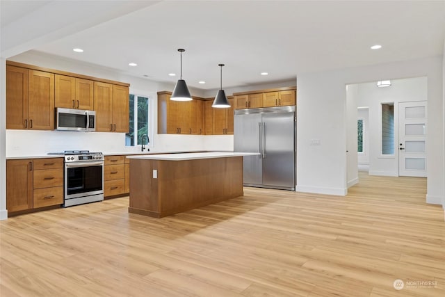 kitchen featuring a kitchen island, hanging light fixtures, appliances with stainless steel finishes, light countertops, and brown cabinetry