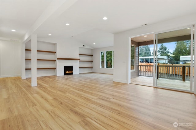 unfurnished living room featuring recessed lighting, vaulted ceiling, a lit fireplace, and light wood finished floors