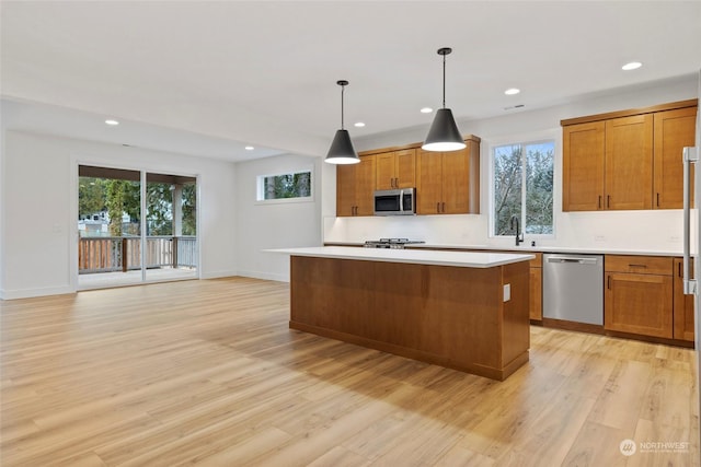 kitchen with stainless steel appliances, a center island, light countertops, brown cabinets, and decorative light fixtures