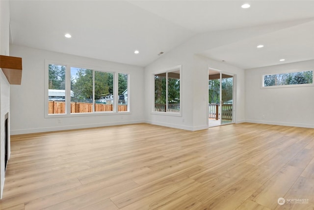 unfurnished living room featuring a healthy amount of sunlight, light wood-style flooring, a fireplace, and vaulted ceiling