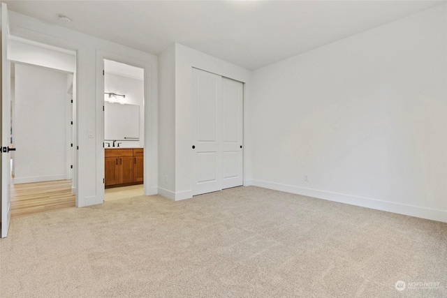 unfurnished bedroom with baseboards, a closet, connected bathroom, and light colored carpet