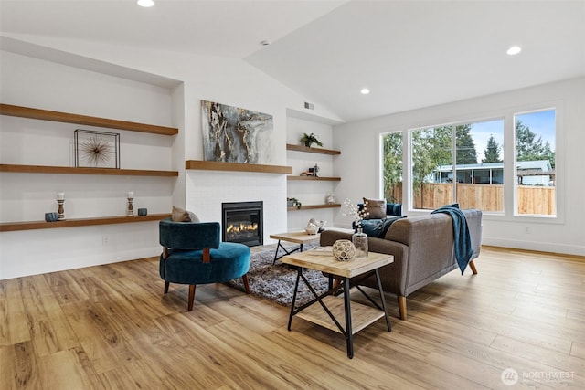 living room with lofted ceiling, recessed lighting, a glass covered fireplace, and light wood-style floors