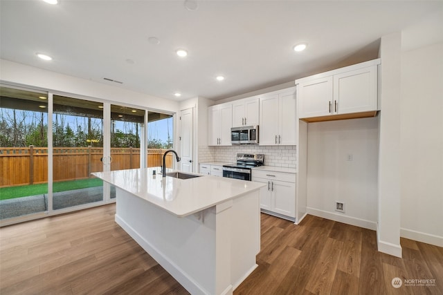 kitchen with sink, appliances with stainless steel finishes, an island with sink, decorative backsplash, and white cabinets