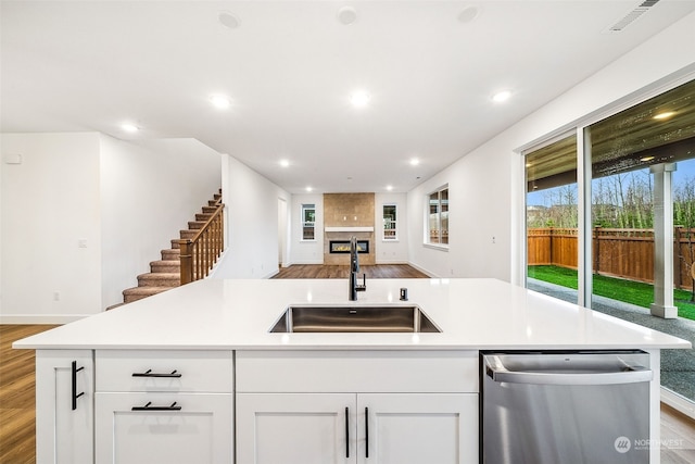 kitchen featuring a kitchen island with sink, sink, stainless steel dishwasher, and white cabinets