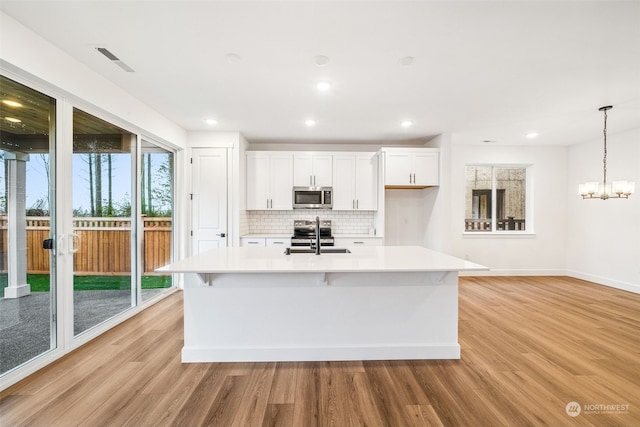 kitchen with white cabinetry, stainless steel appliances, an island with sink, and pendant lighting