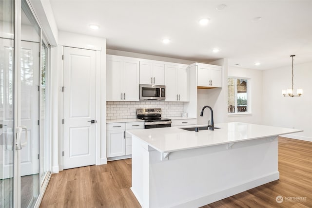 kitchen with sink, appliances with stainless steel finishes, white cabinets, a center island with sink, and decorative light fixtures