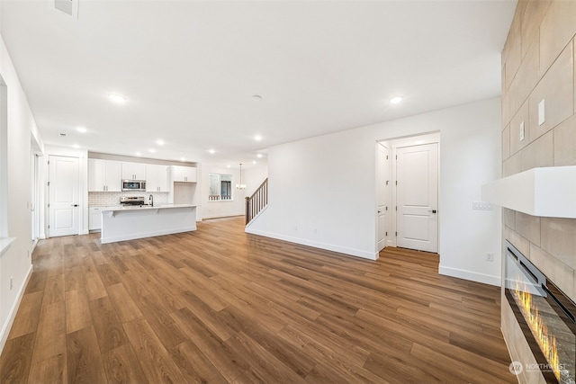 unfurnished living room featuring a tiled fireplace, sink, and light hardwood / wood-style flooring