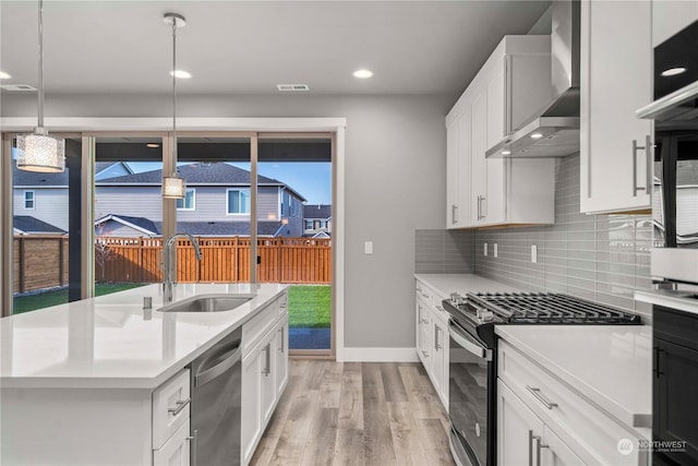 kitchen with wall chimney exhaust hood, sink, pendant lighting, stainless steel appliances, and white cabinets