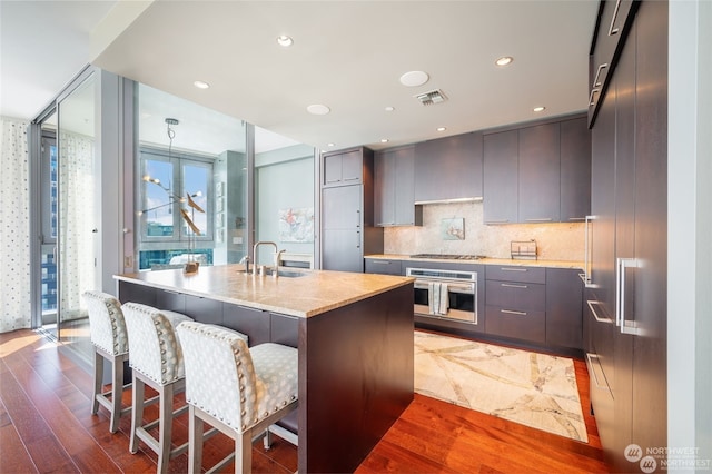 kitchen featuring sink, backsplash, a kitchen island with sink, stainless steel appliances, and dark wood-type flooring