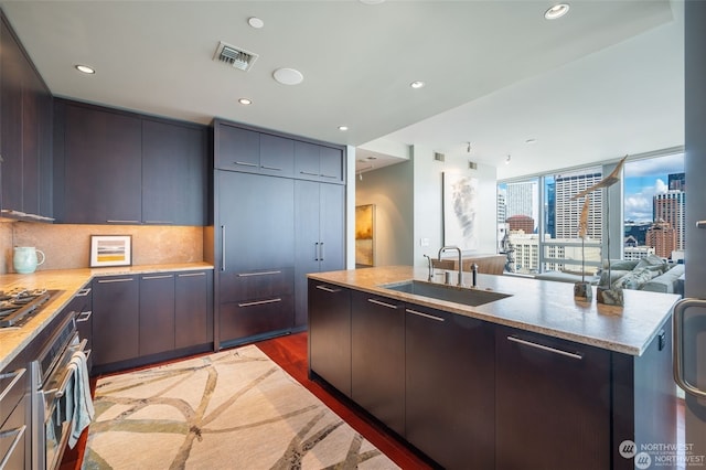 kitchen with tasteful backsplash, an island with sink, sink, stainless steel appliances, and dark wood-type flooring