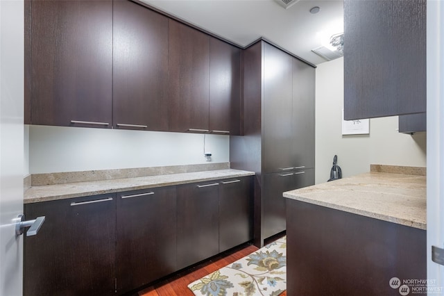 kitchen featuring light stone counters, dark brown cabinetry, and light hardwood / wood-style flooring