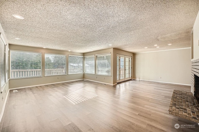 unfurnished living room featuring a brick fireplace, light hardwood / wood-style floors, french doors, and a textured ceiling