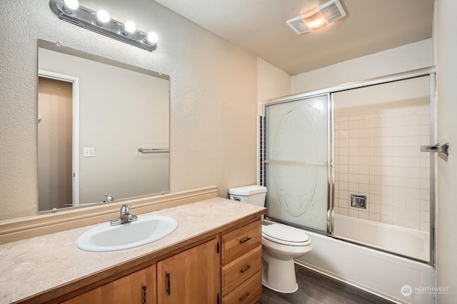 full bathroom with hardwood / wood-style floors, vanity, toilet, and bath / shower combo with glass door