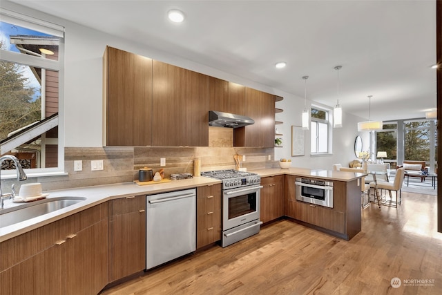 kitchen featuring pendant lighting, sink, stainless steel appliances, exhaust hood, and kitchen peninsula