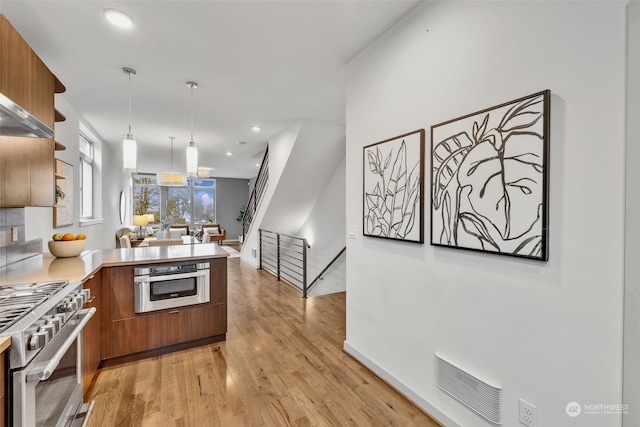 kitchen featuring appliances with stainless steel finishes, kitchen peninsula, hanging light fixtures, and light wood-type flooring