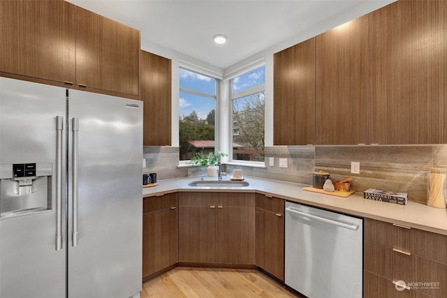 kitchen featuring light wood-type flooring, stainless steel appliances, sink, and backsplash