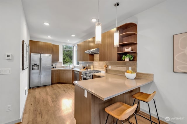 kitchen featuring appliances with stainless steel finishes, tasteful backsplash, a breakfast bar area, hanging light fixtures, and kitchen peninsula