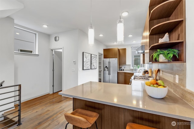 kitchen with wall chimney exhaust hood, high end fridge, sink, kitchen peninsula, and pendant lighting