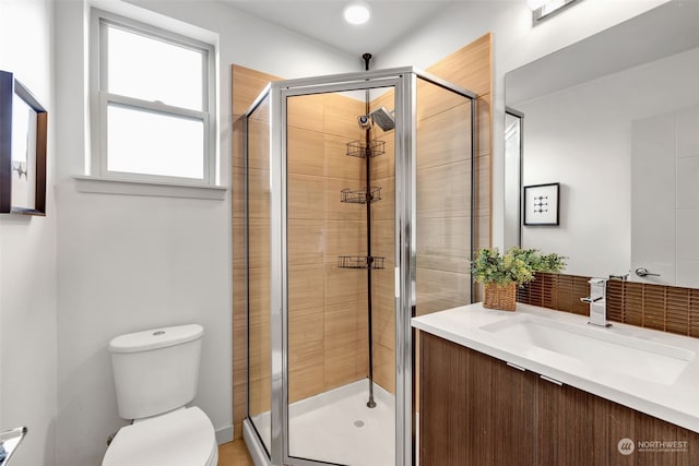 bathroom featuring a shower with door, vanity, and toilet