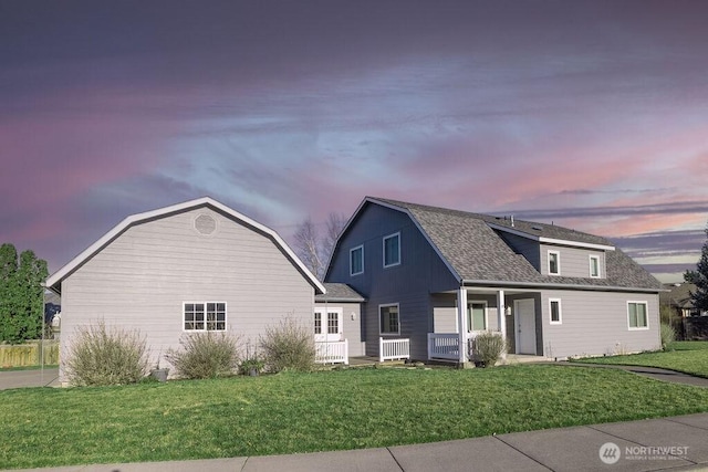 colonial inspired home with a yard, a porch, roof with shingles, and a gambrel roof